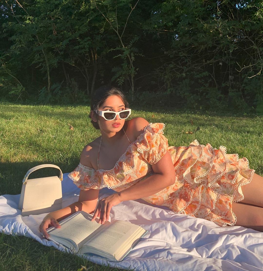 woman reading a book on a picnic blanket in a floral dress with ruffles