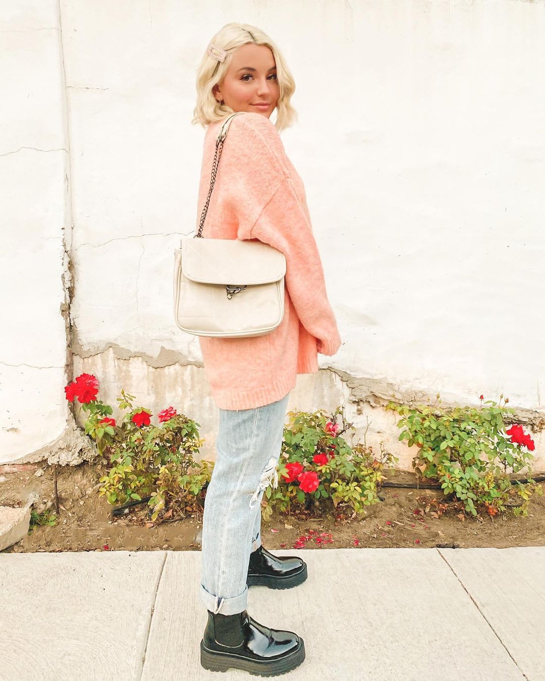 woman wearing an oversized pink sweater with a shoulder bag and cuffed distressed jeans with patent boots