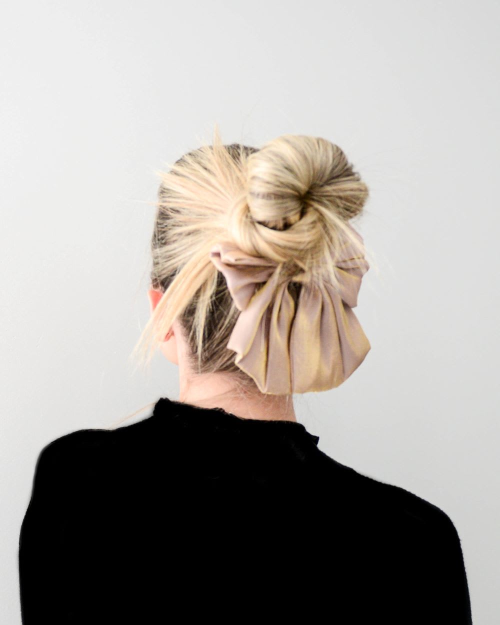 back view of a woman wearing a black top and a messy bun with a bow