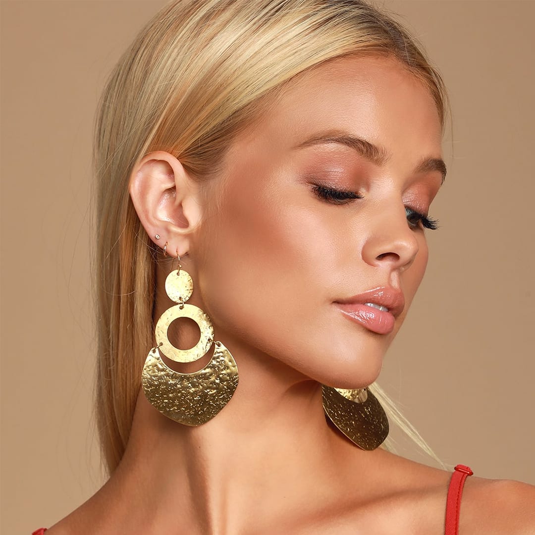 a blonde woman looking down wearing gold hammered 70s inspired earrings