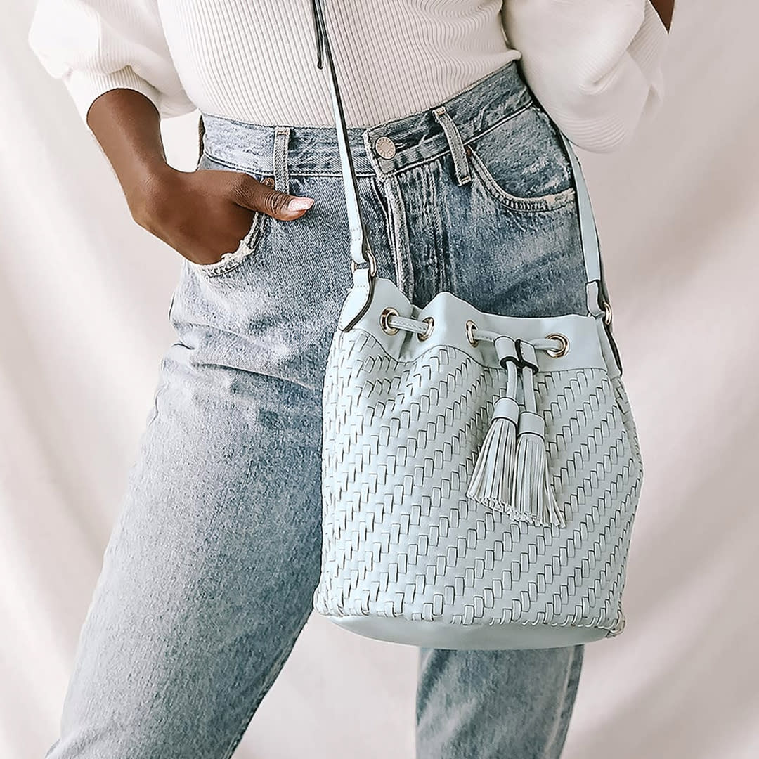 a light blue woven bucket bag resting on a womans hip in jeans