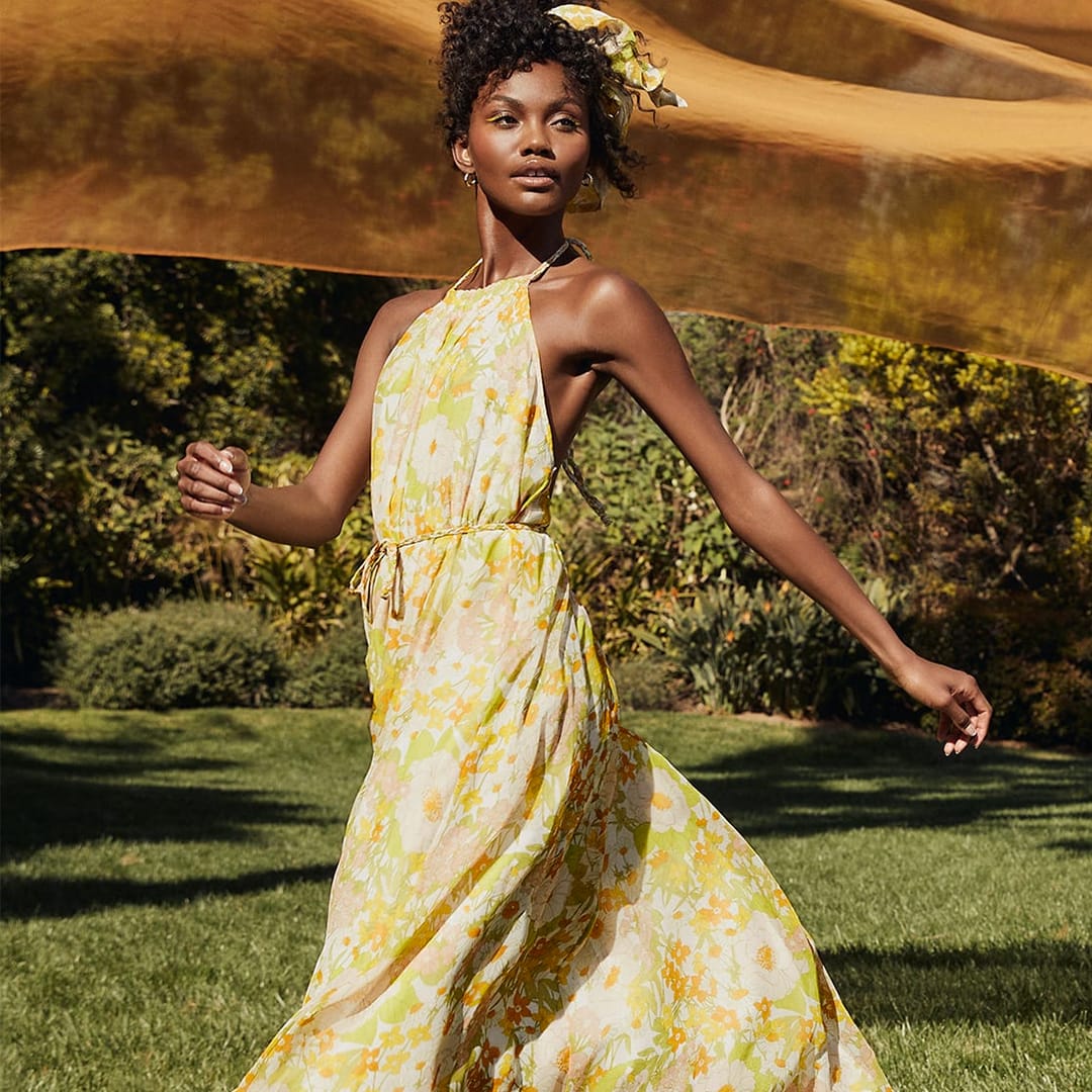 a model running across the grass wearing a green multi floral print halter maxi dress in 70s trend