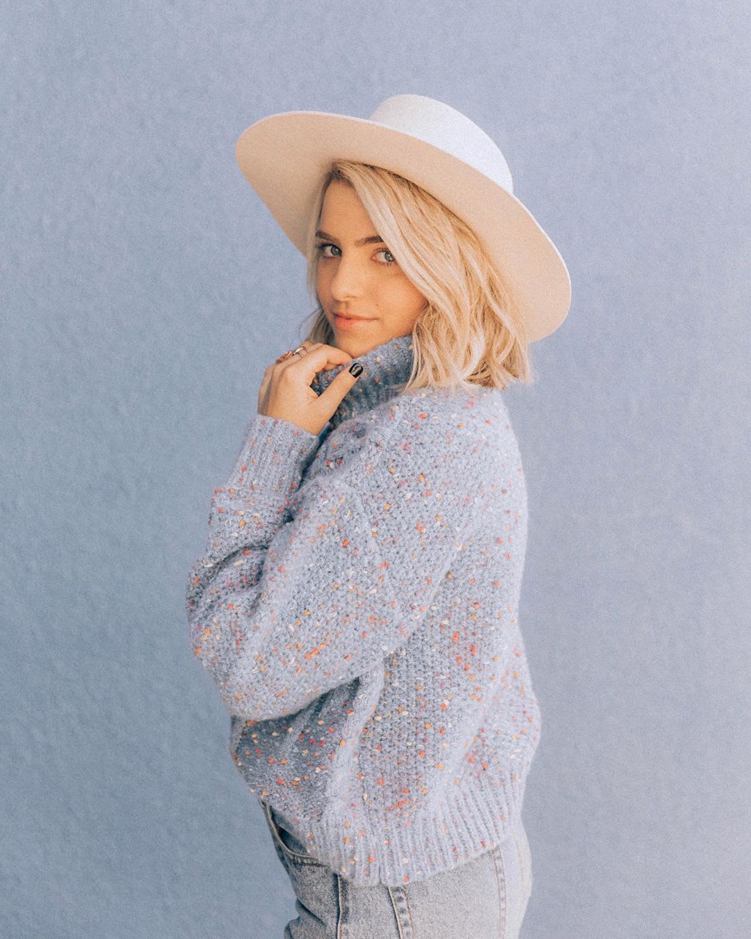 blonde woman in blue sweater and fedora as example of winter skincare