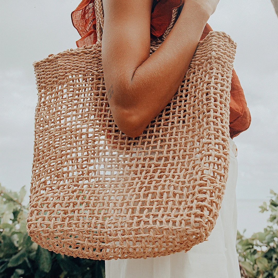 a woman on the beach with a beige woven tote on her arm