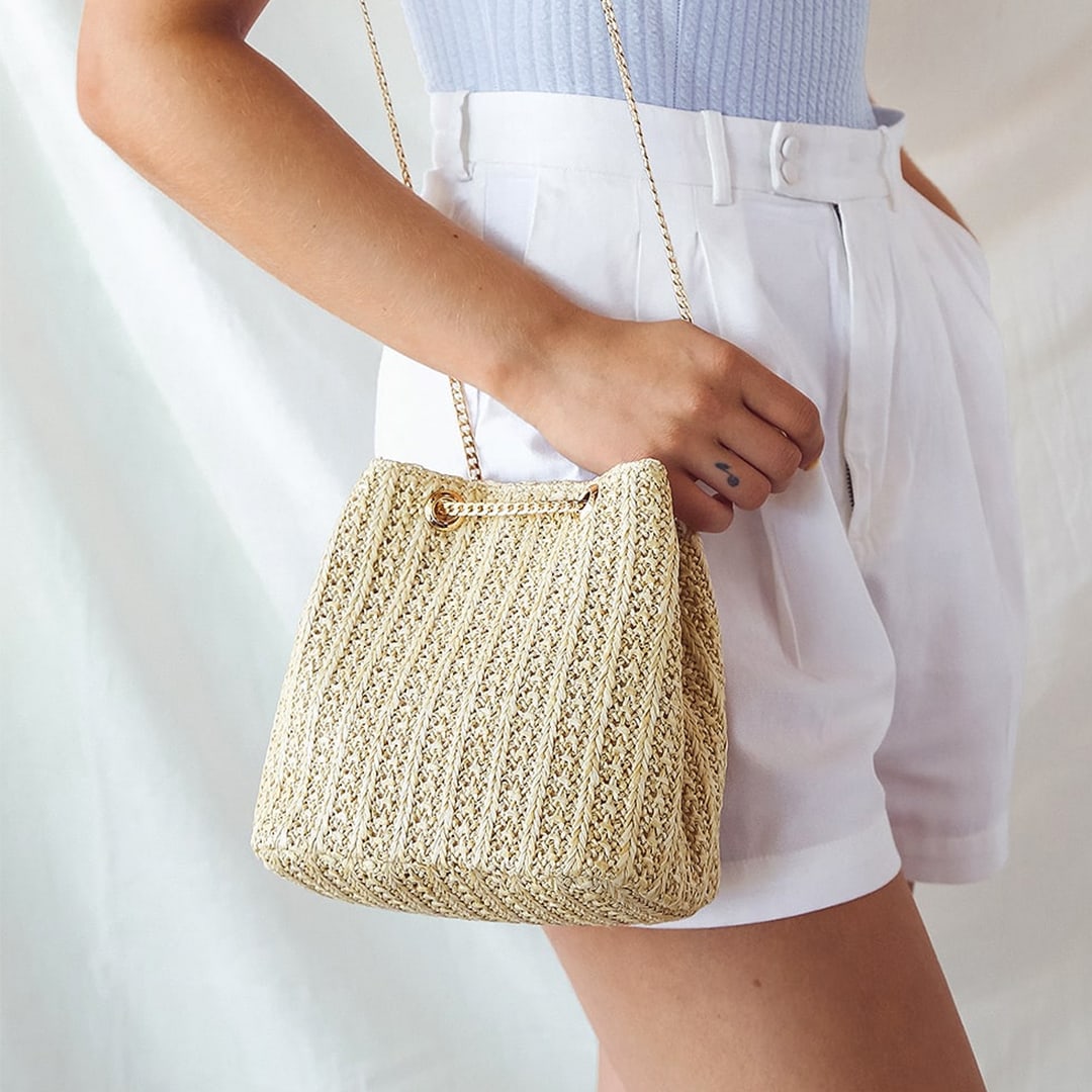 detail shot of a woman in white shorts with her hand on a straw mini bag with a gold chain strap