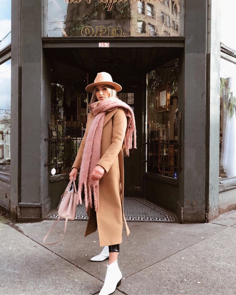 a woman wearing a camel coat, blush pink scarf, and white boots outfit