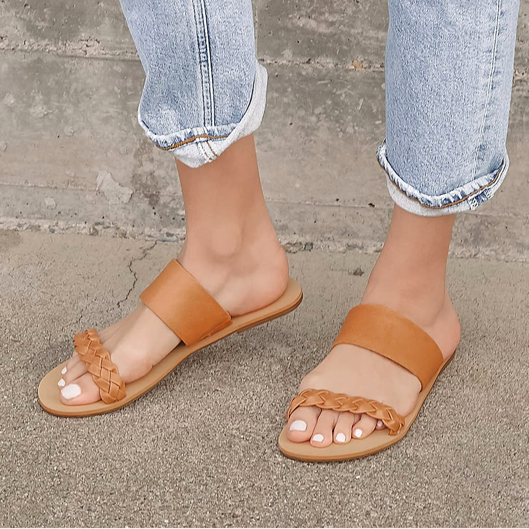 feet wearing brown leather slide sandals with braiding