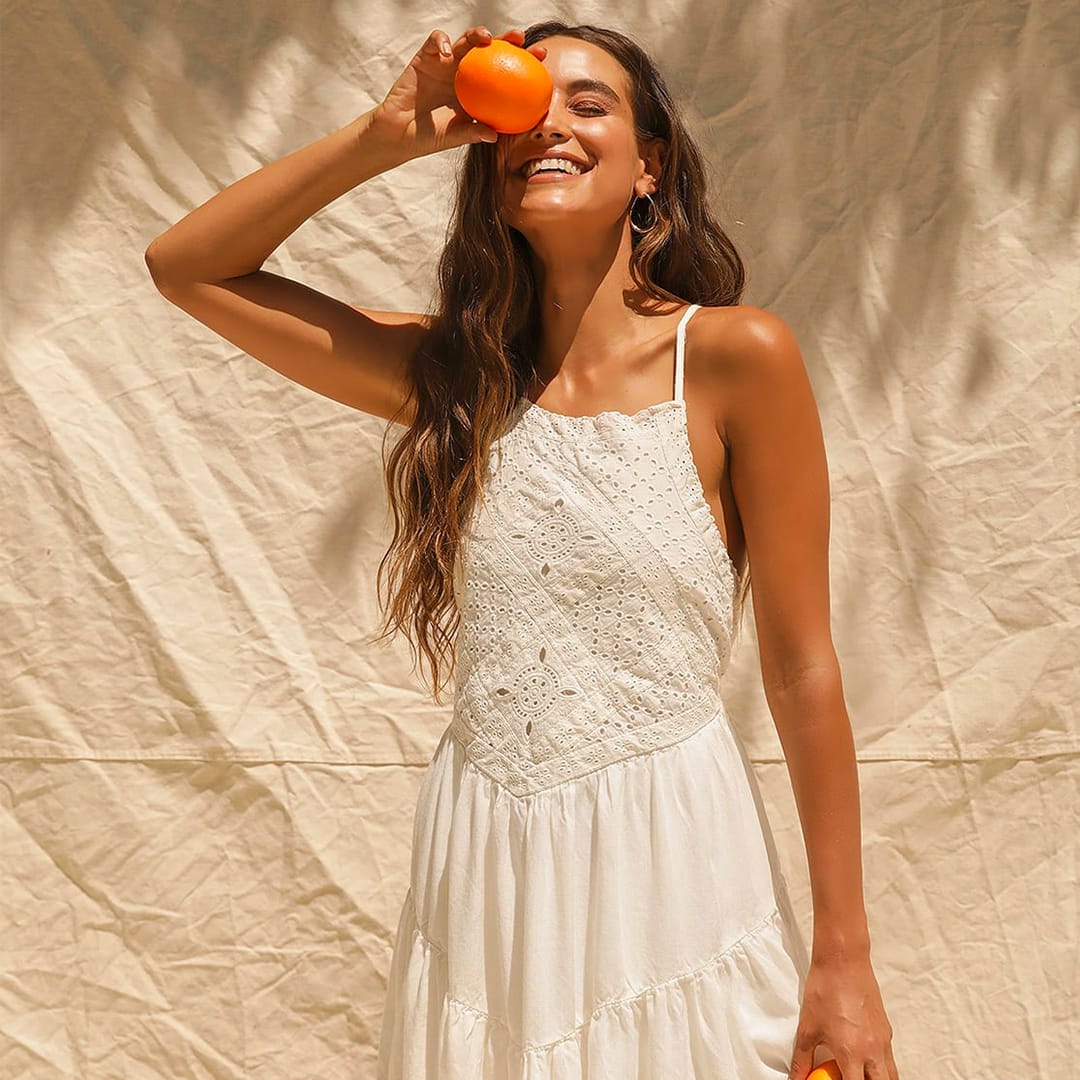 model wearing a cream eyelet lace mini dress holding an orange over her eye