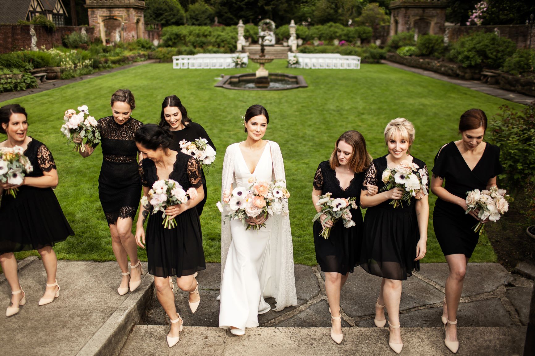bride in white cape gown with bridal party in black short bridesmaid dresses