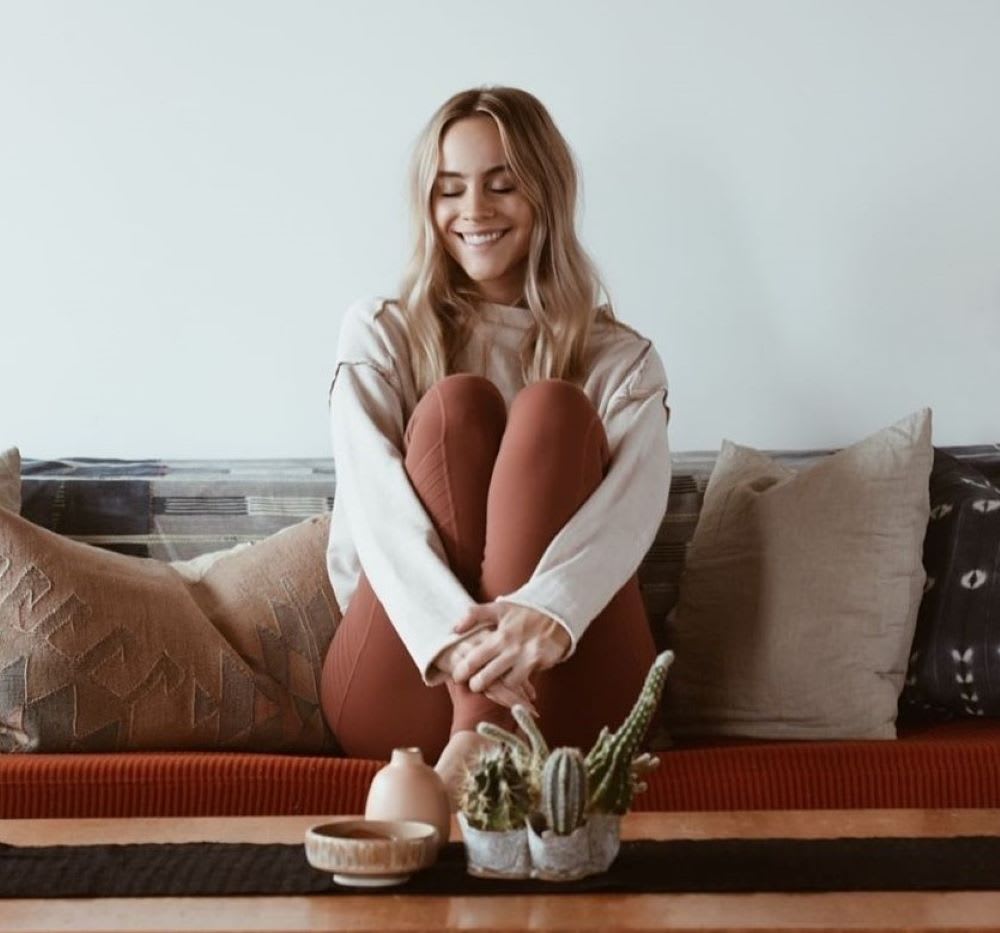 blonde woman sitting on couch holding her legs to her chest