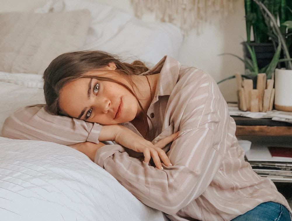 brunette woman laying her head in her hands on a bed