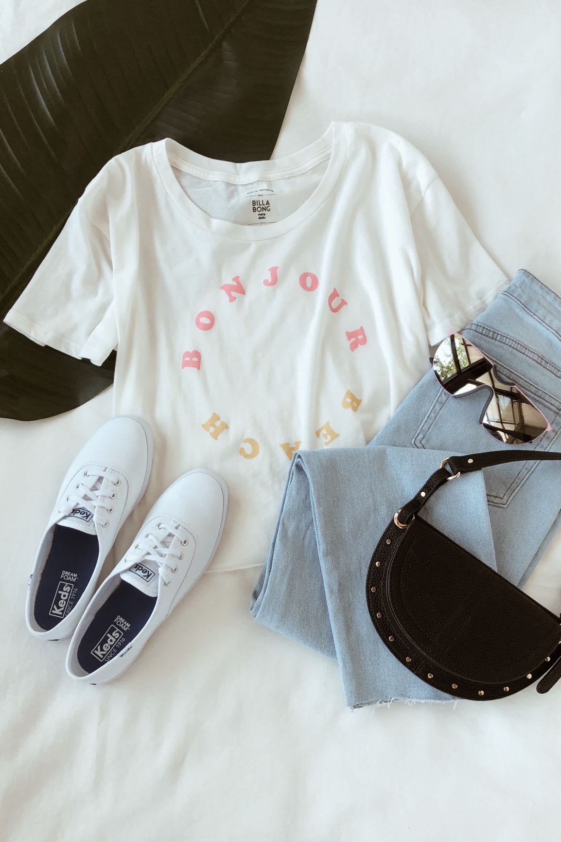 white bojour beach tee with light wash jeans and shield sunglasses and sneakers and black belt bag for how to wear a graphic tee
