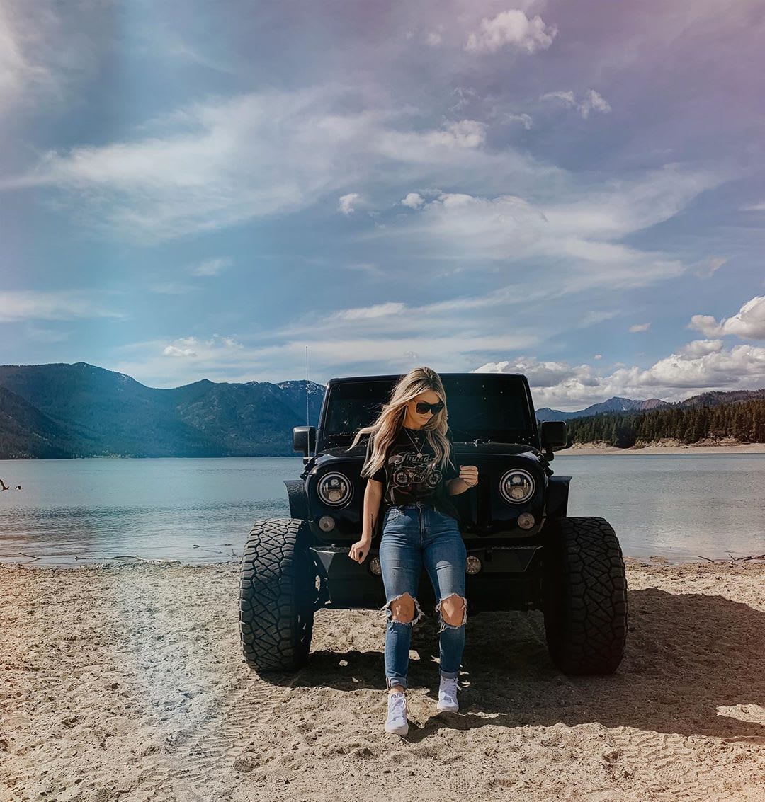 woman in jeans and graphic tee sitting on the back of a truck at the beach