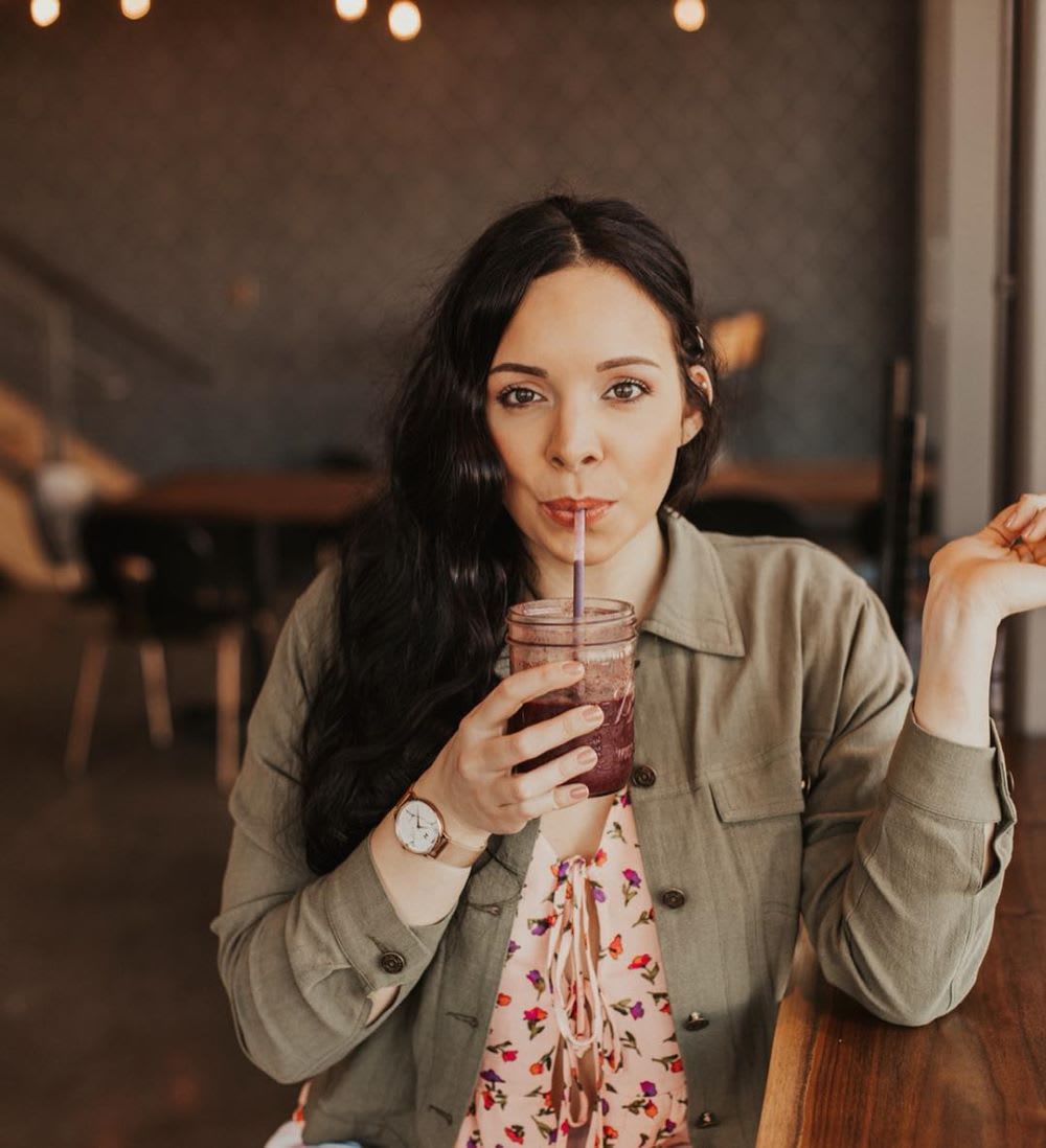 woman sipping a red drink from a mason jar