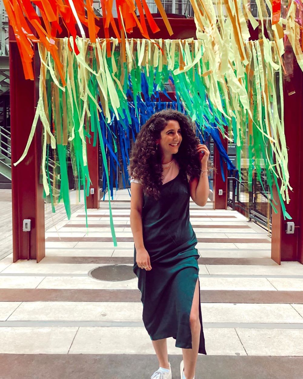 woman in green slip dress walking under rainbow streamers for world pride 2019