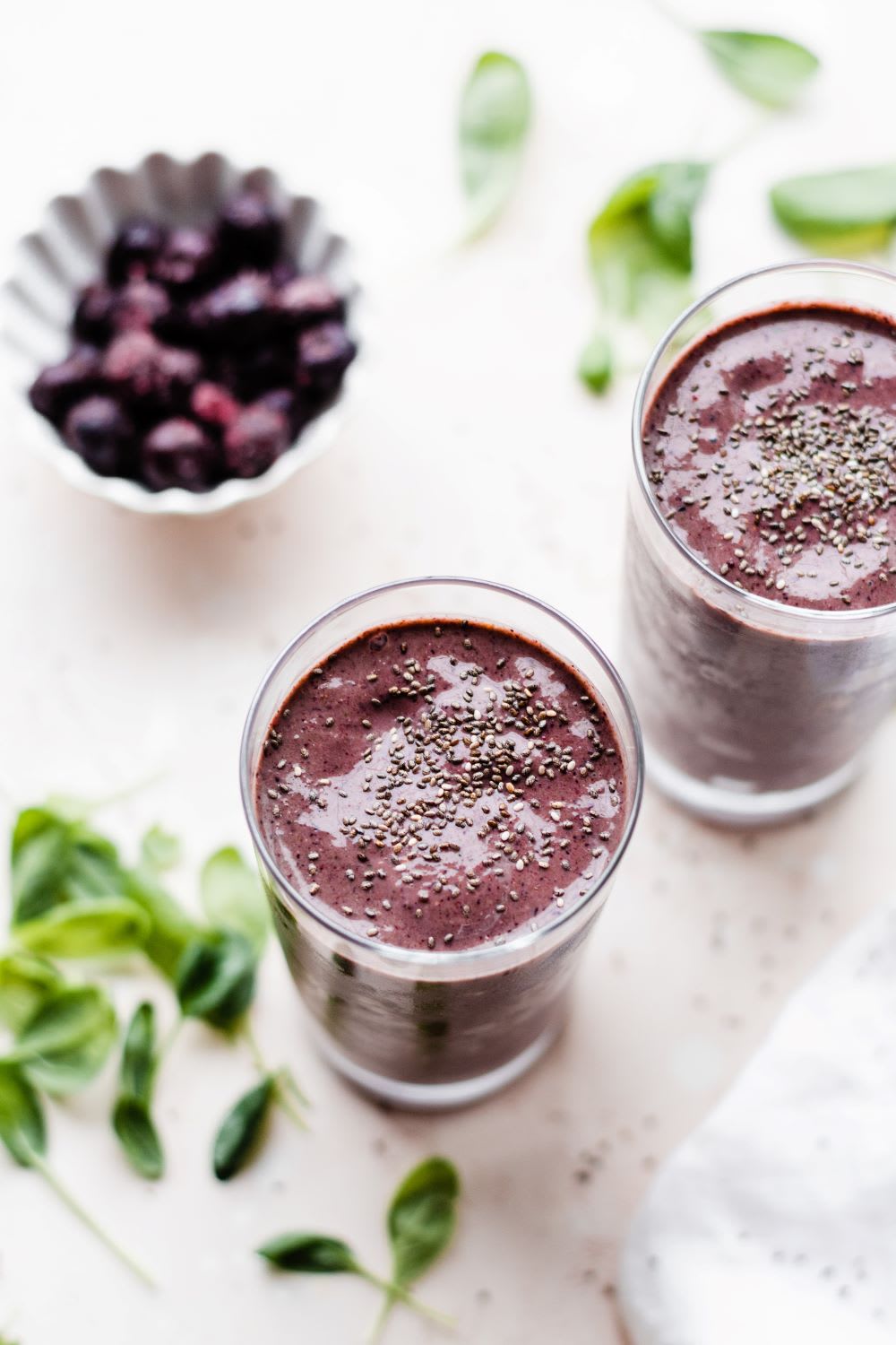 berry spinach smoothie in two glasses with leaves around 