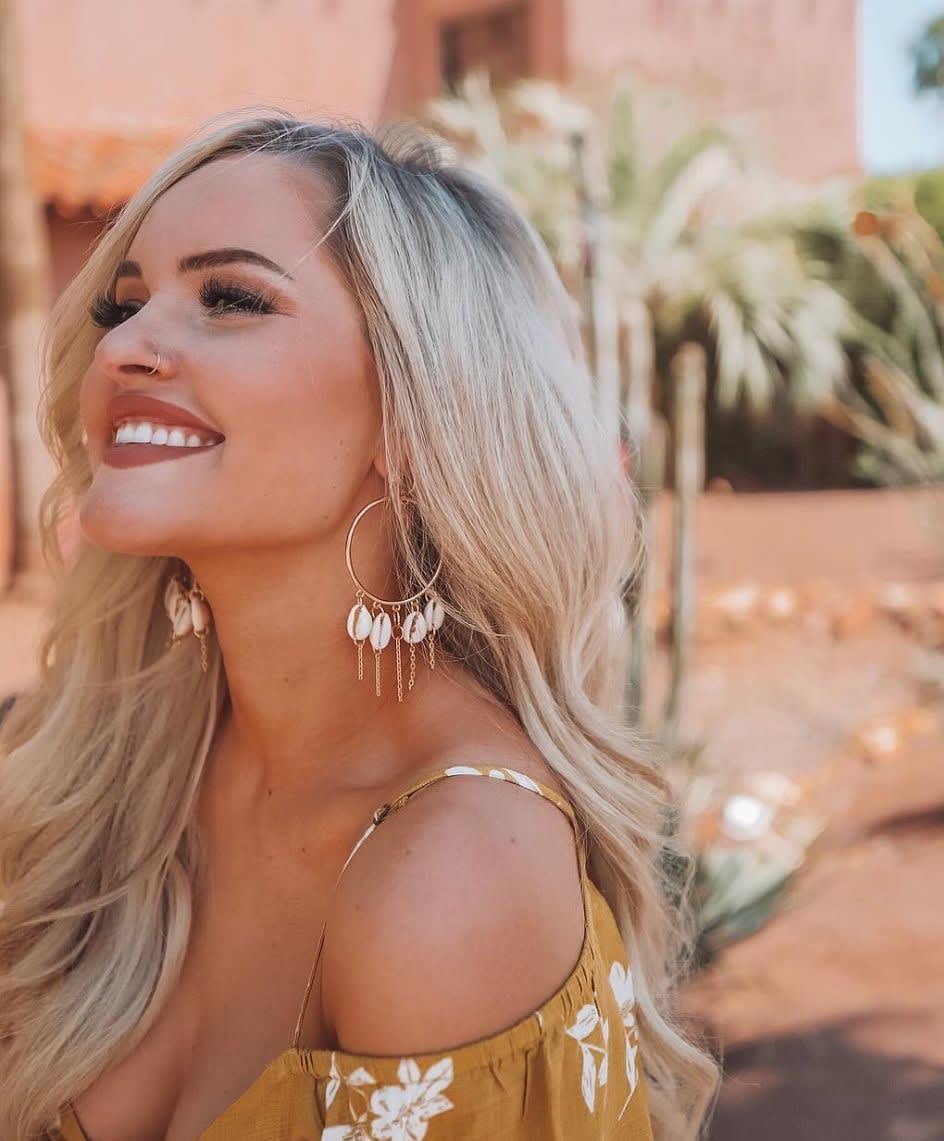 blonde woman smiling while wearing gold cowrie shell hoop earrings