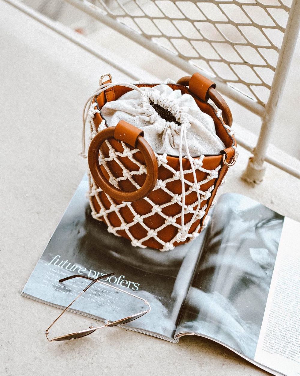 a brown tote bag with white netting on a magazine with sunglasses nearby