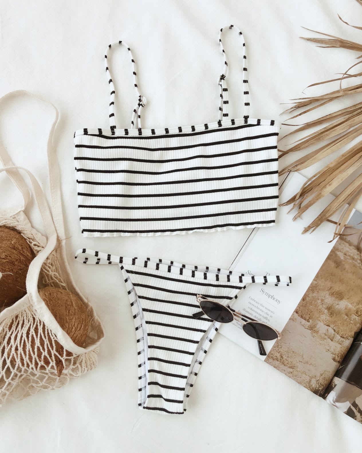 white and black striped tankini top and bikini bottom on a white background next to a net tote and small sunglasses