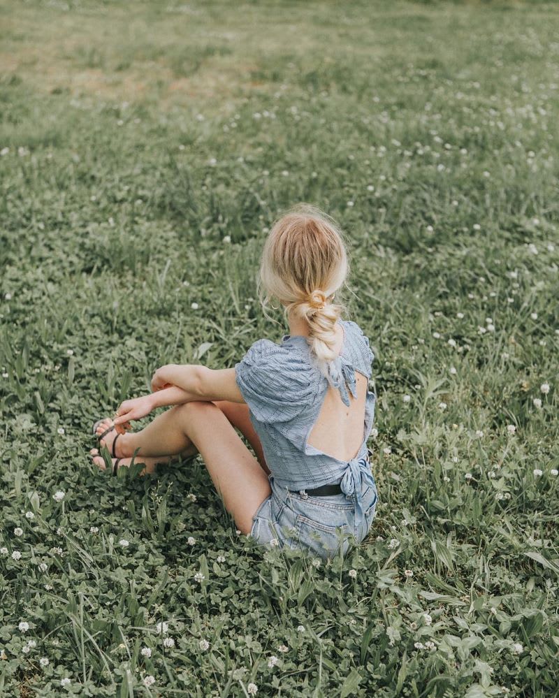 back view of blonde woman in backless shirt and shorts sitting on the grass