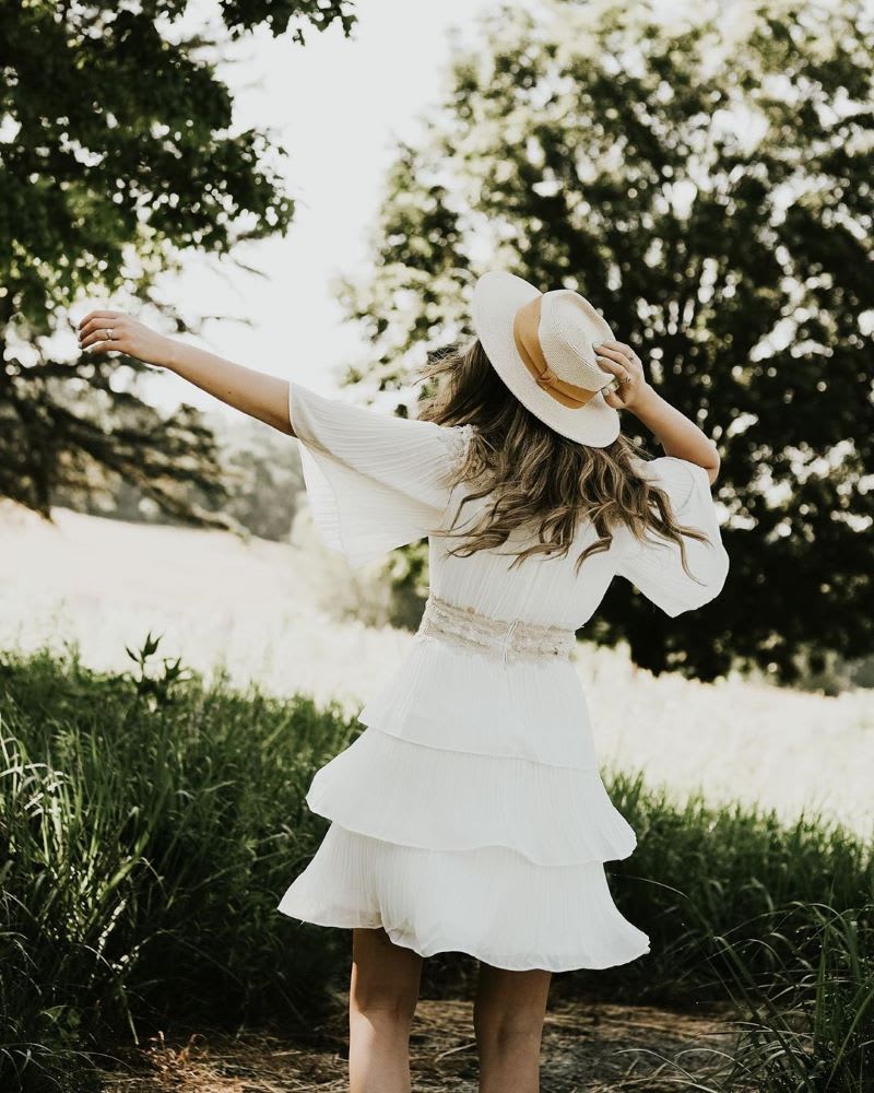 woman twirling in a white dress and sun hat outside as summer wellness tip