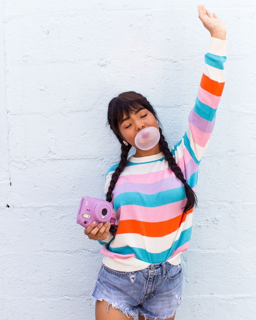 woman in mutlicolor stripe sweater and denim shorts holding a camera with one arm in the air for feminist podcasts