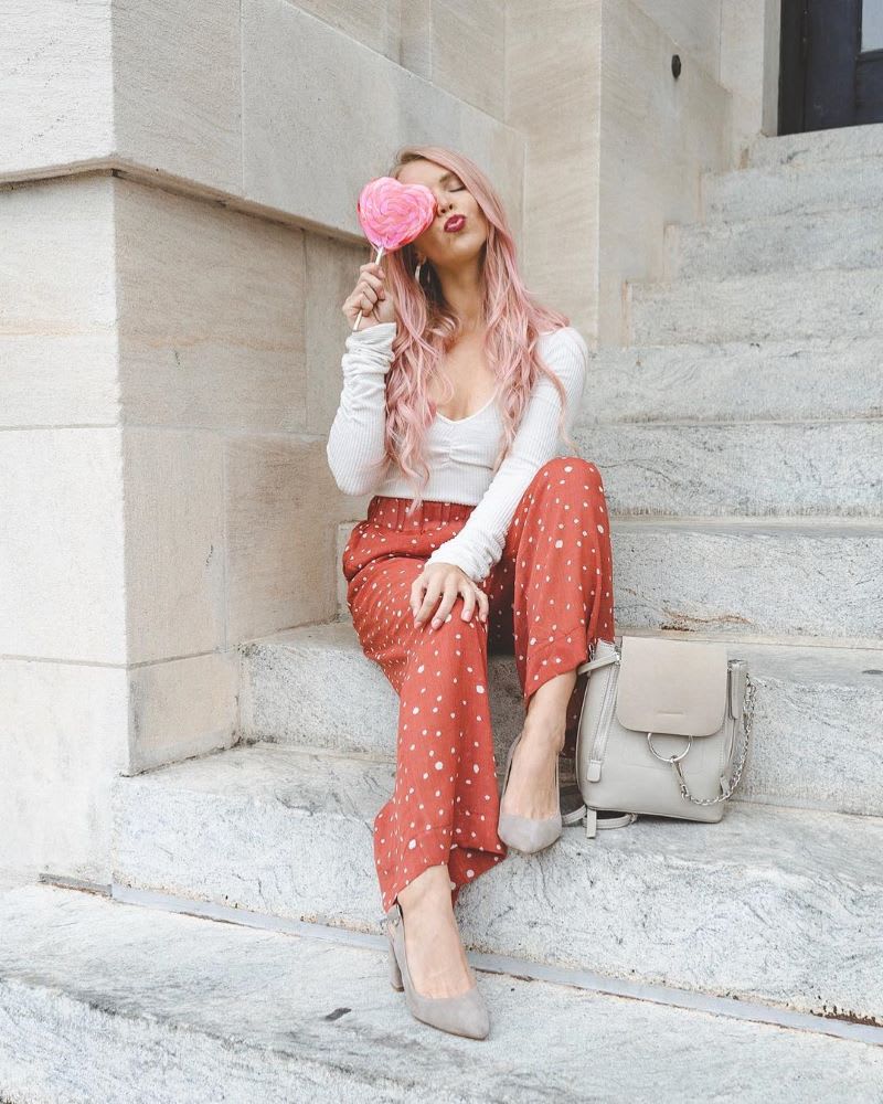 woman with pink hair holding heart lollipop in front of her face