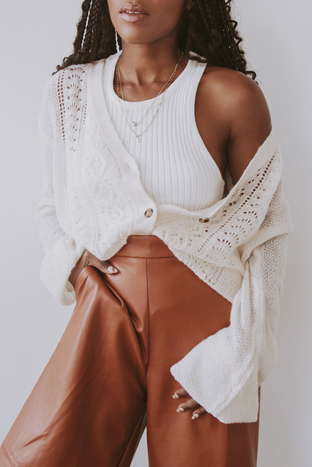 woman wearing a white tank and cardigan with brown vegan leather pants