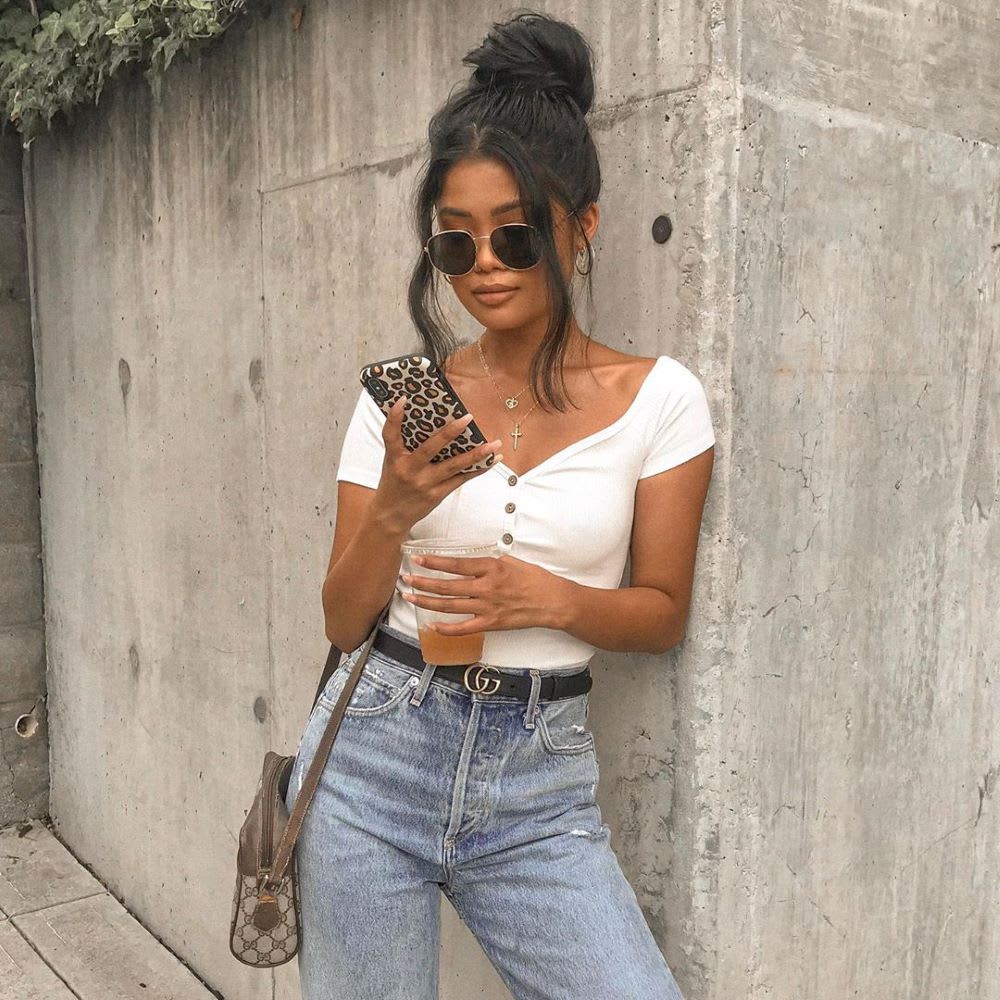woman in white top and jeans looking at her phone