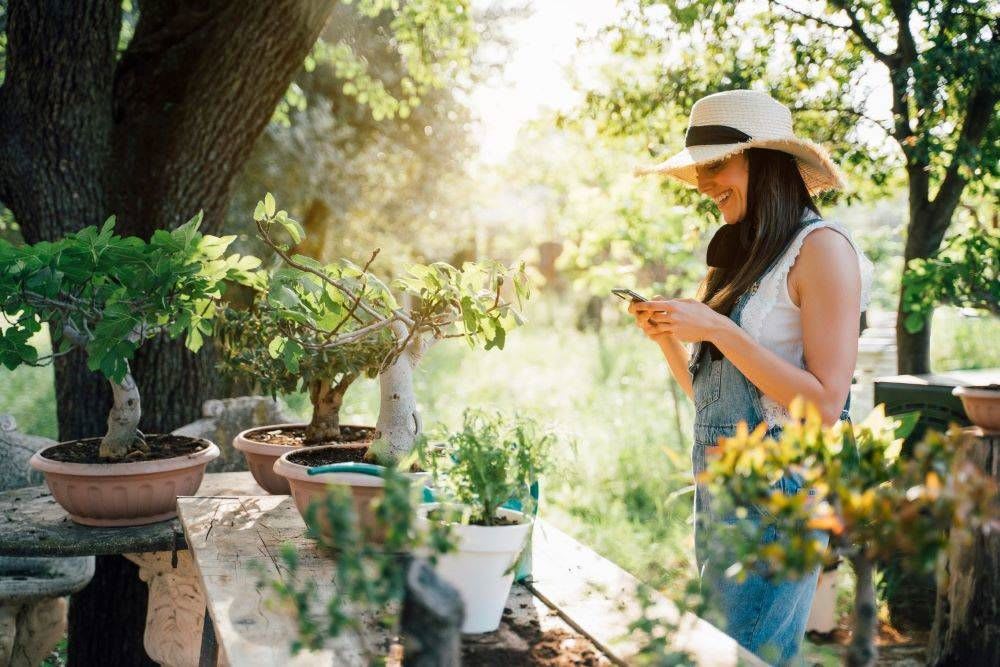 woman in garden wearing denim overalls and straw hat caring for bonsai trees