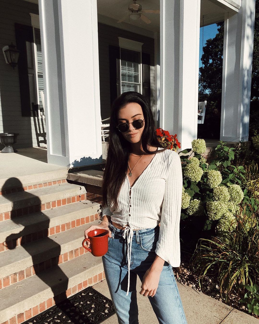 woman in white top and jeans holding a mug