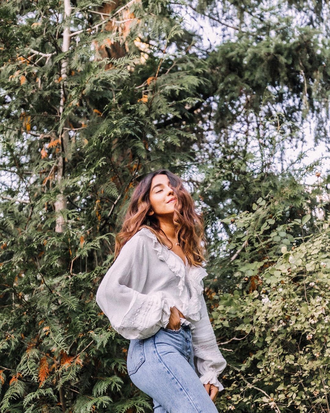 woman in white top and jeans in front of trees