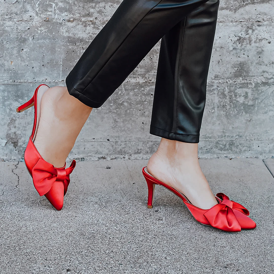 detail of black leather pants clad legs wearing red satin bow mules for valentines day