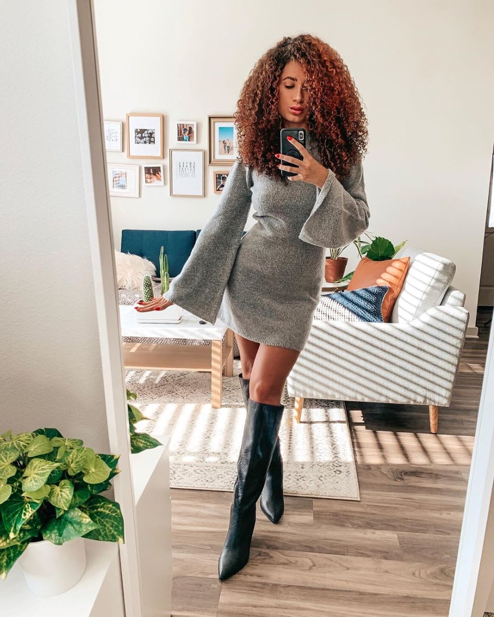 woman holding phone in the mirror wearing a sweater dress and boots