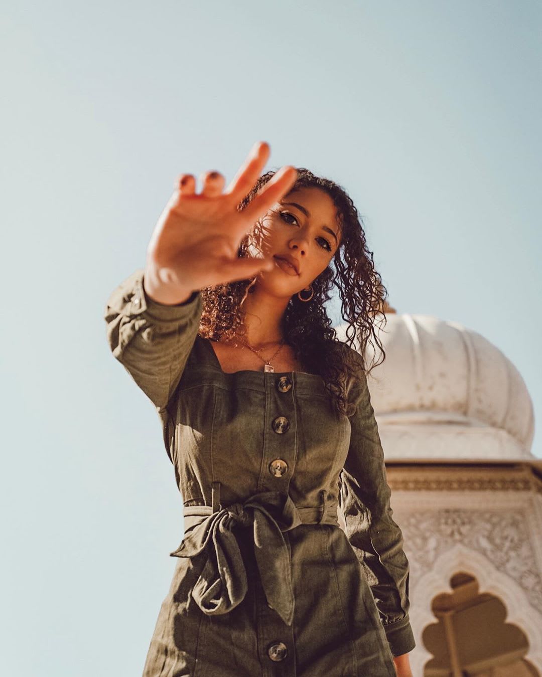 woman in green button front dress raising hand to camera