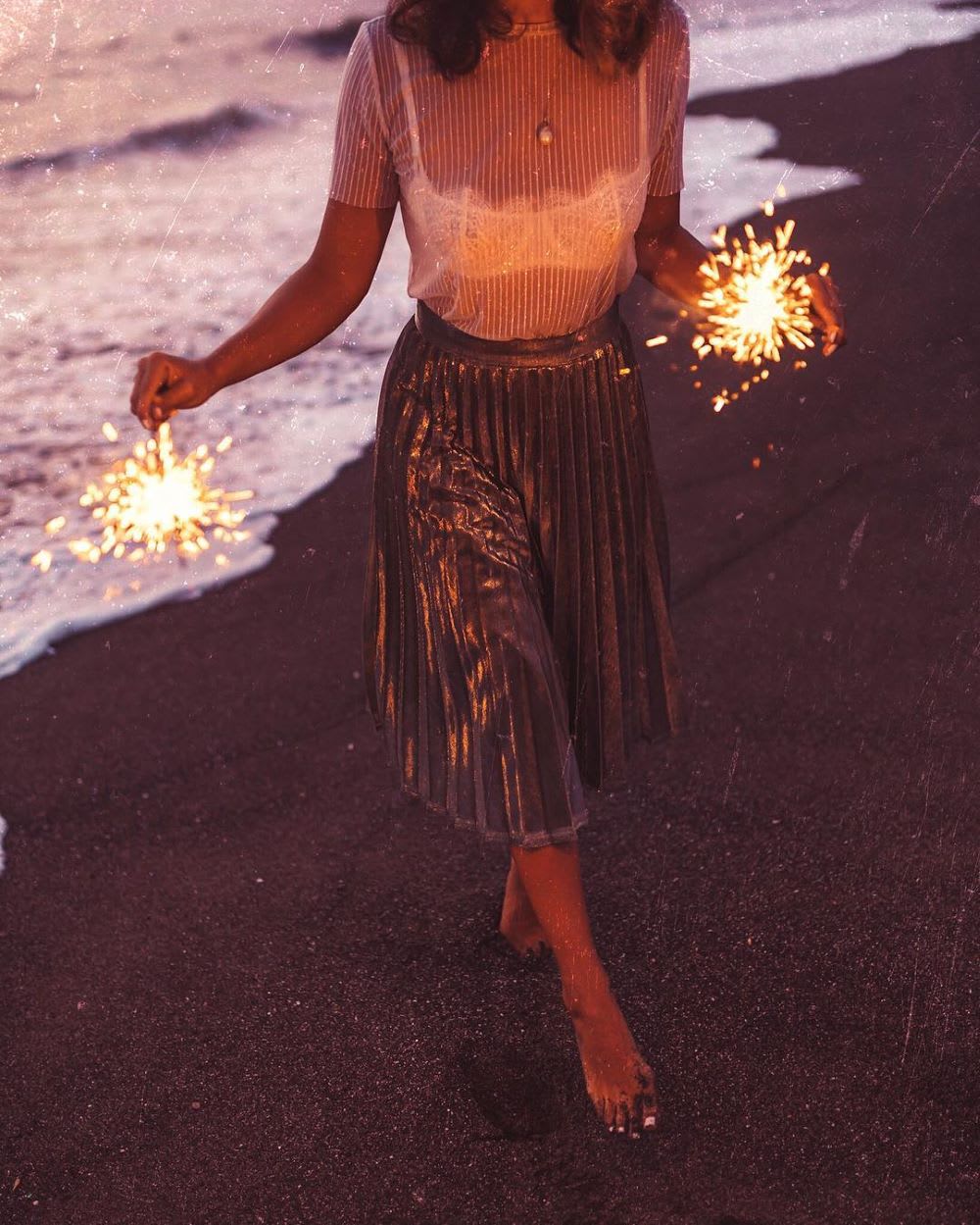 woman in pleated gold skirt with sparklers making new year goals