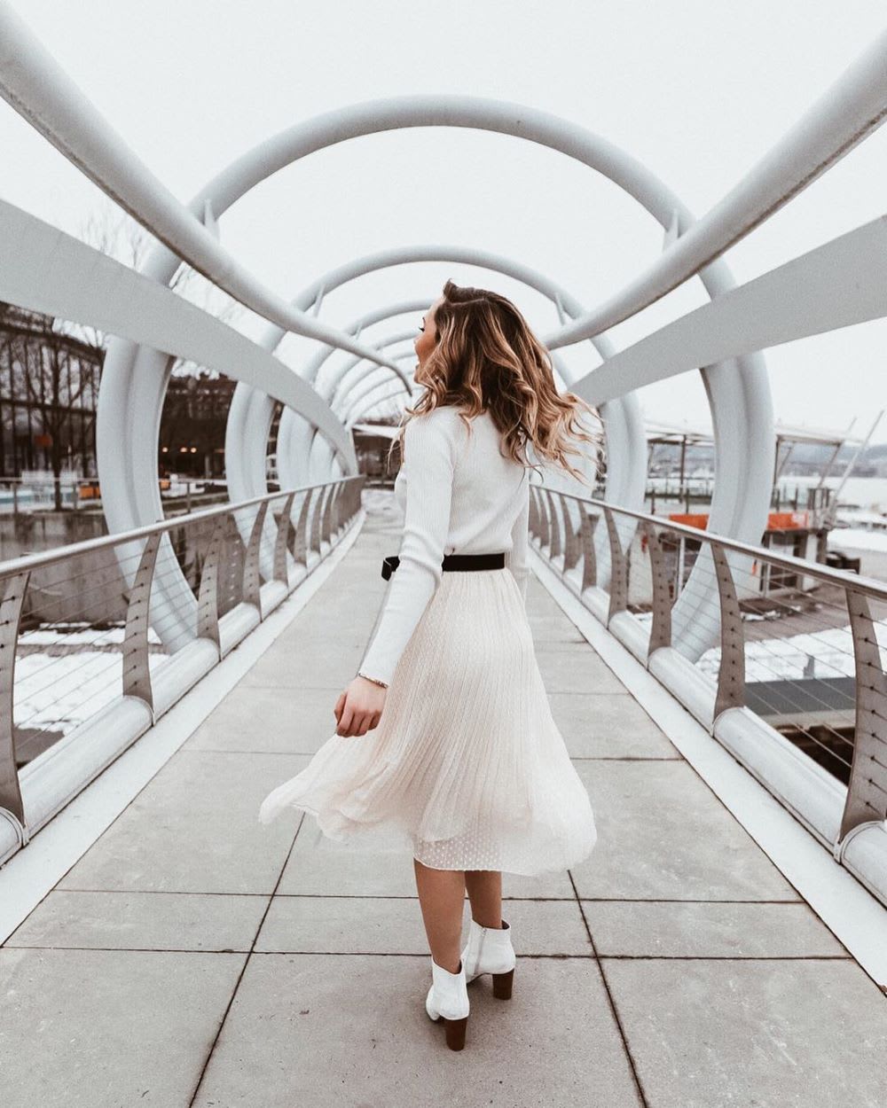 woman in white boots and pleated midi skirt walking away