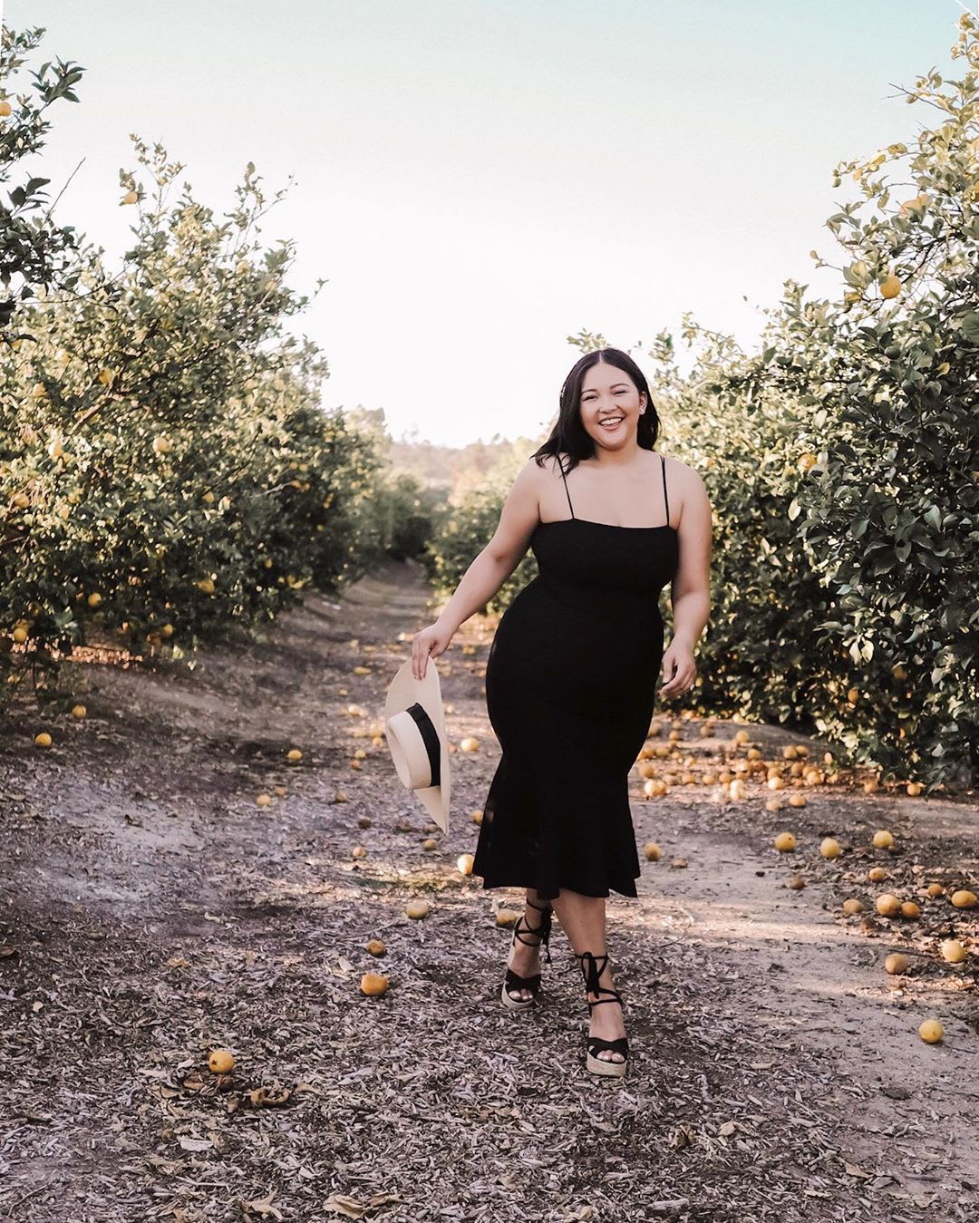 woman in black dress walking through apple orchard