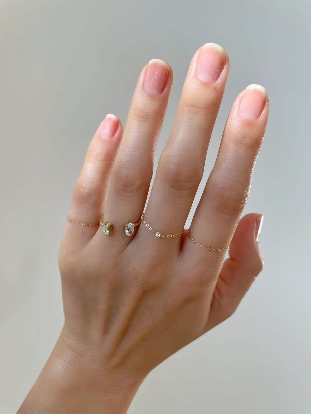 a hand with nude nails and clear nail polish and gold rings