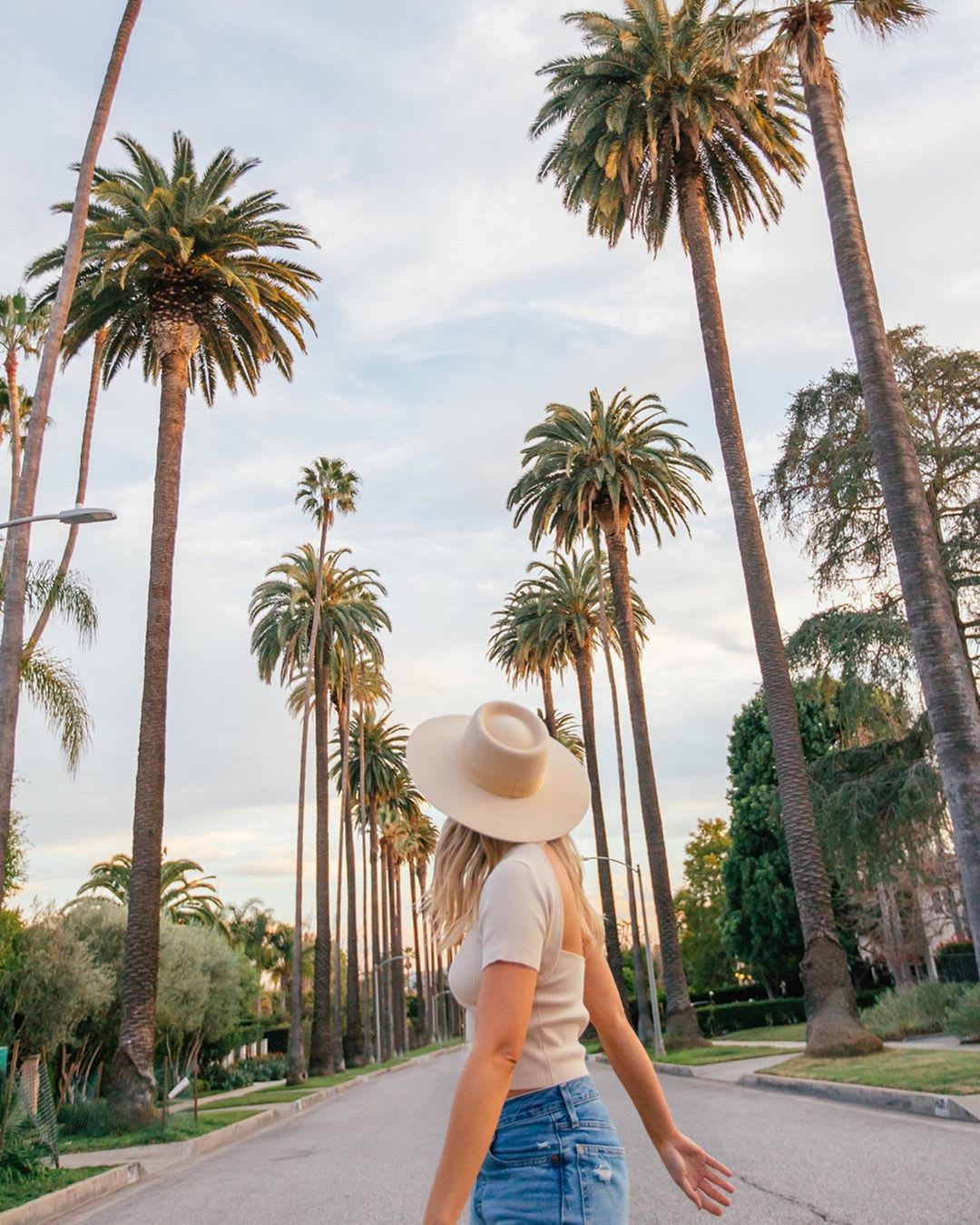 woman in hat walking down street with palm trees