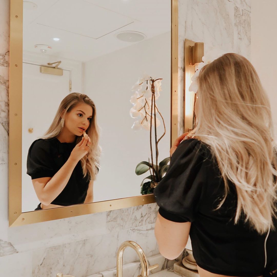 woman putting on makeup in the mirror at home