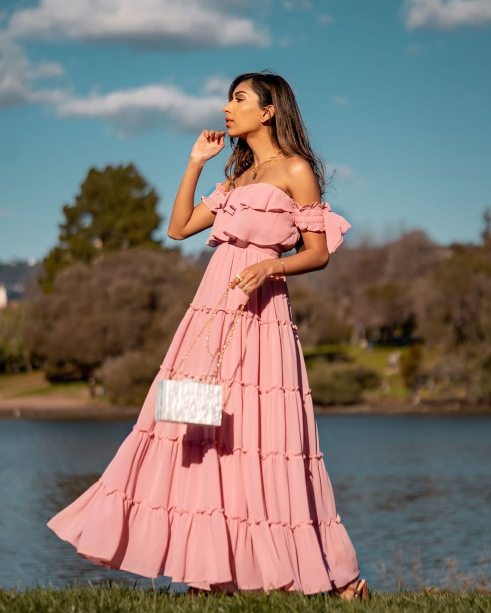 a woman wearing a pink tiered off the shoulder maxi dress holding a box clutch with a chain strap