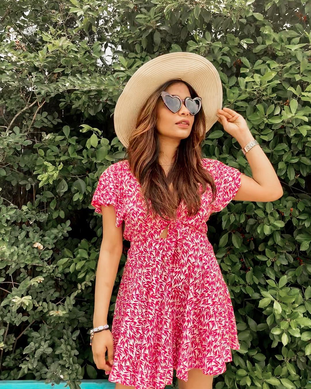 woman with a sun hat, sunglasses, and hair blowout in a floral dress