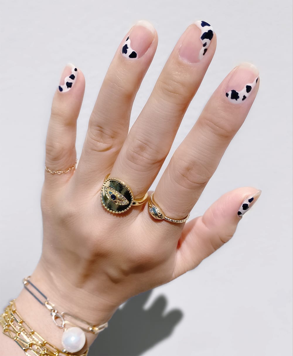 hand with cow print nails and gold jewelry