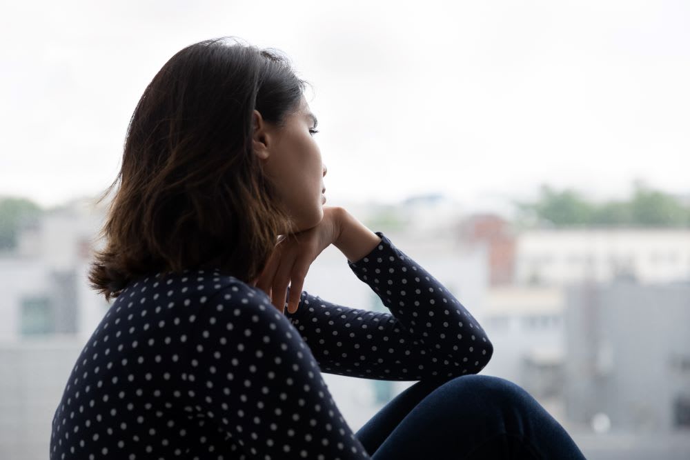 woman with re-entry anxiety looking thoughtfullly out the window with her head in her hand