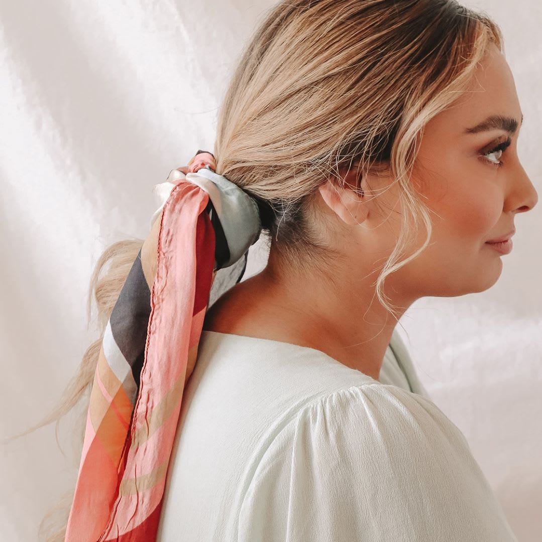 a profile of a woman with a low ponytail and a multicolor hair scarf