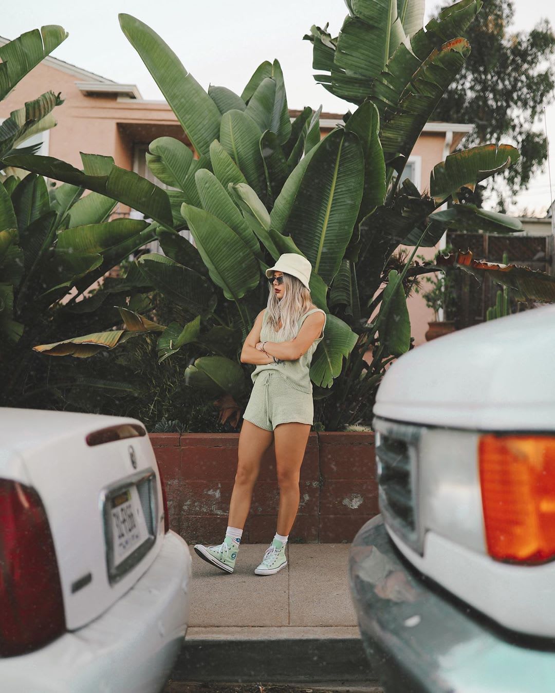 blonde woman in a hat and knit matching set waiting on the sidewalk with crossed arms