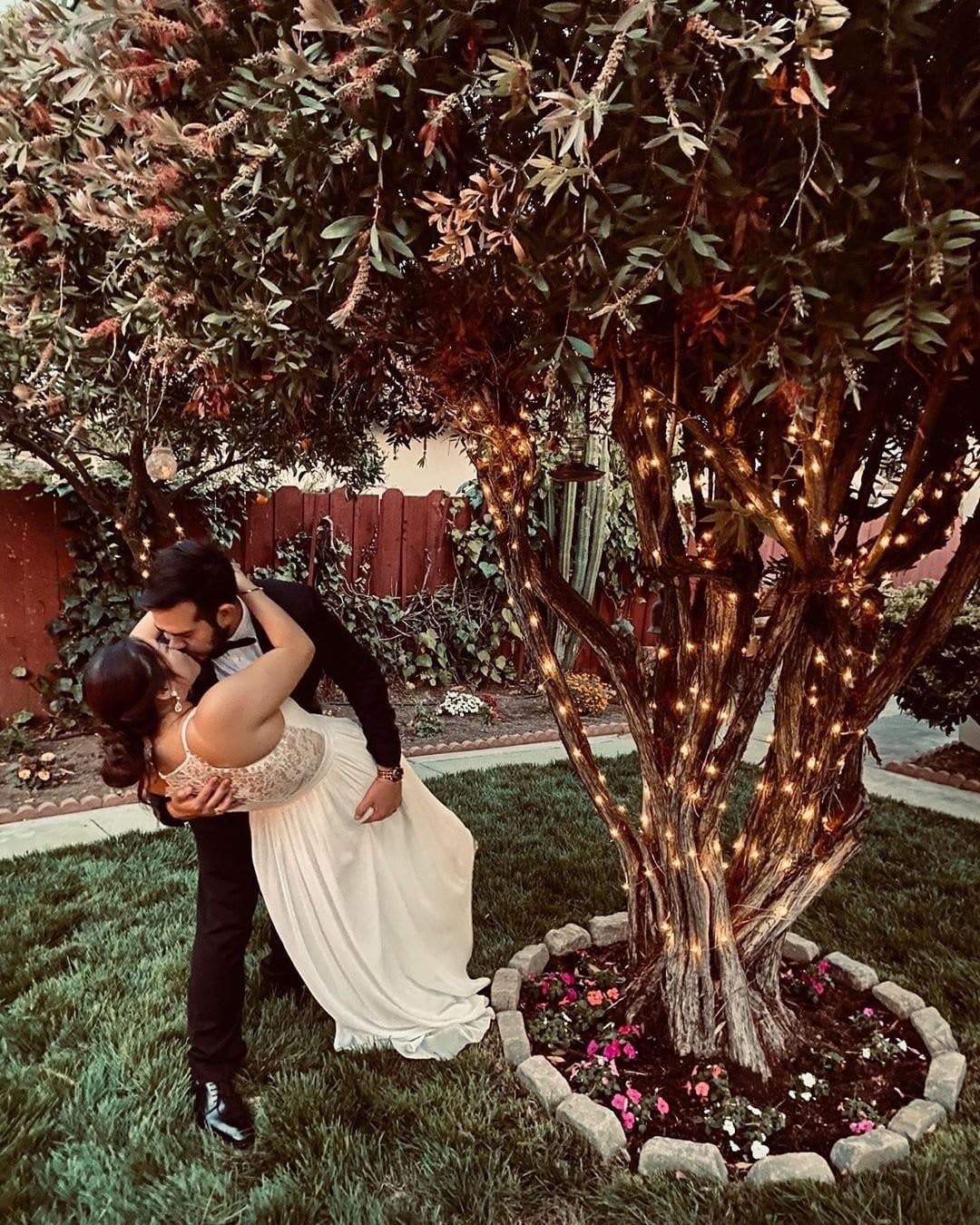 bride and groom kissing under a tree with string lights at backyard wedding