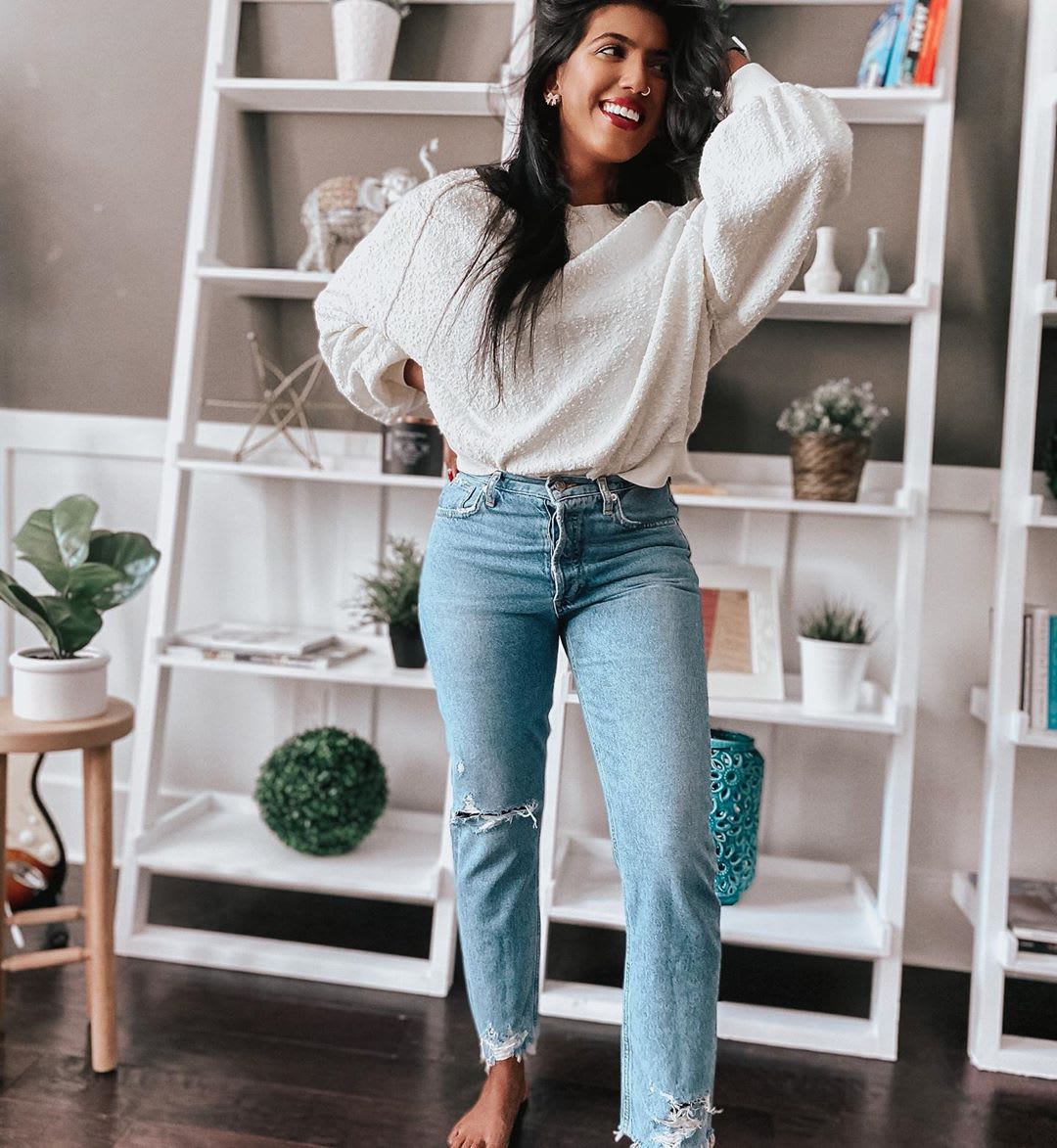 woman wearing a sweater and jeans with hand in hair thinking about savings 
