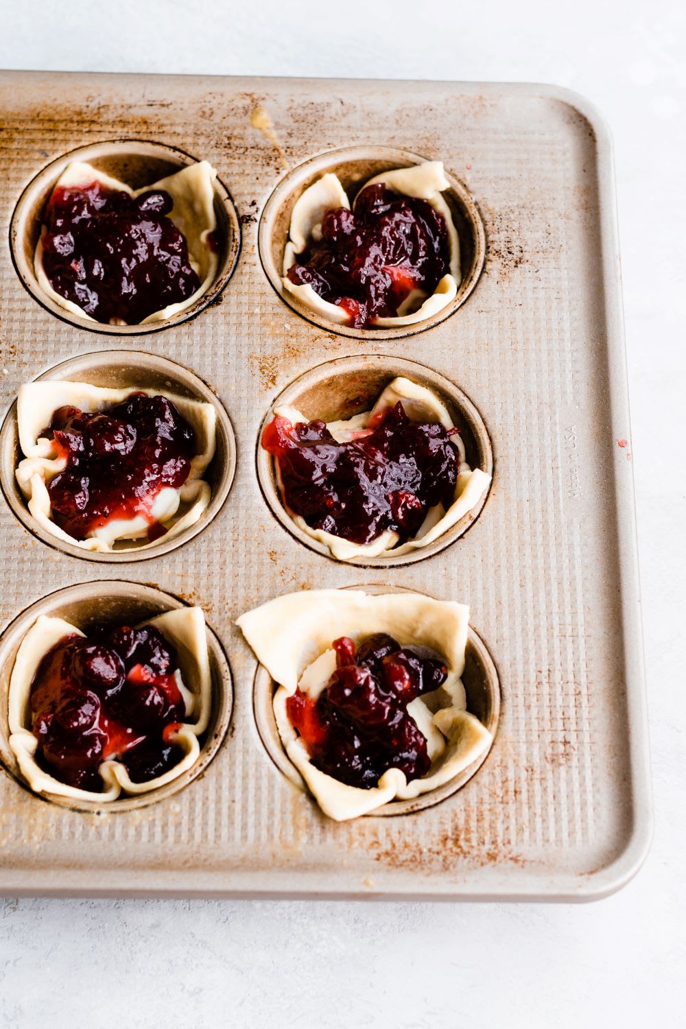 cranberry sauce, brie, and pastry dough in muffin tin